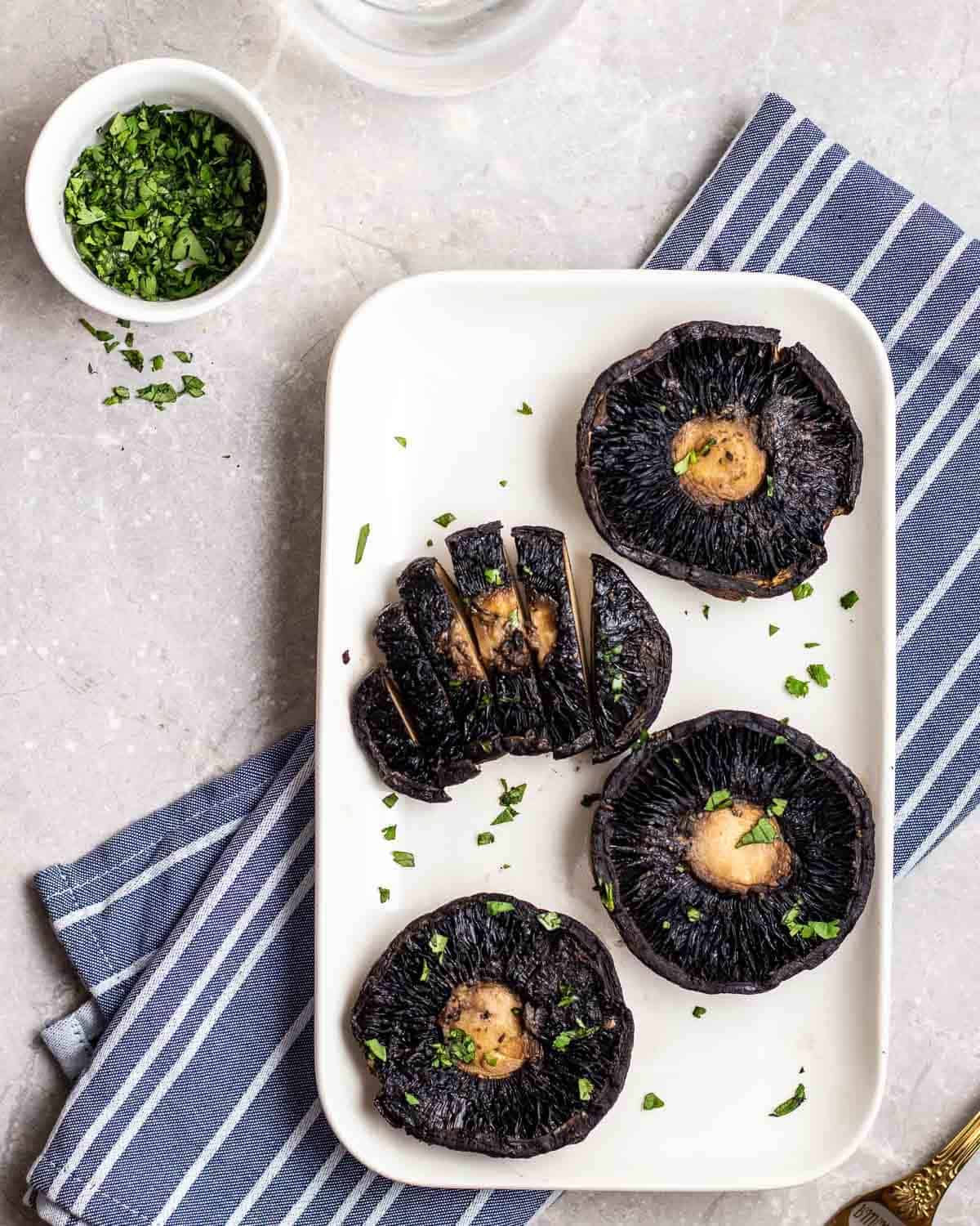 4 portobello mushrooms on a plate topped with chopped cilantro on a blue striped teacloth. 