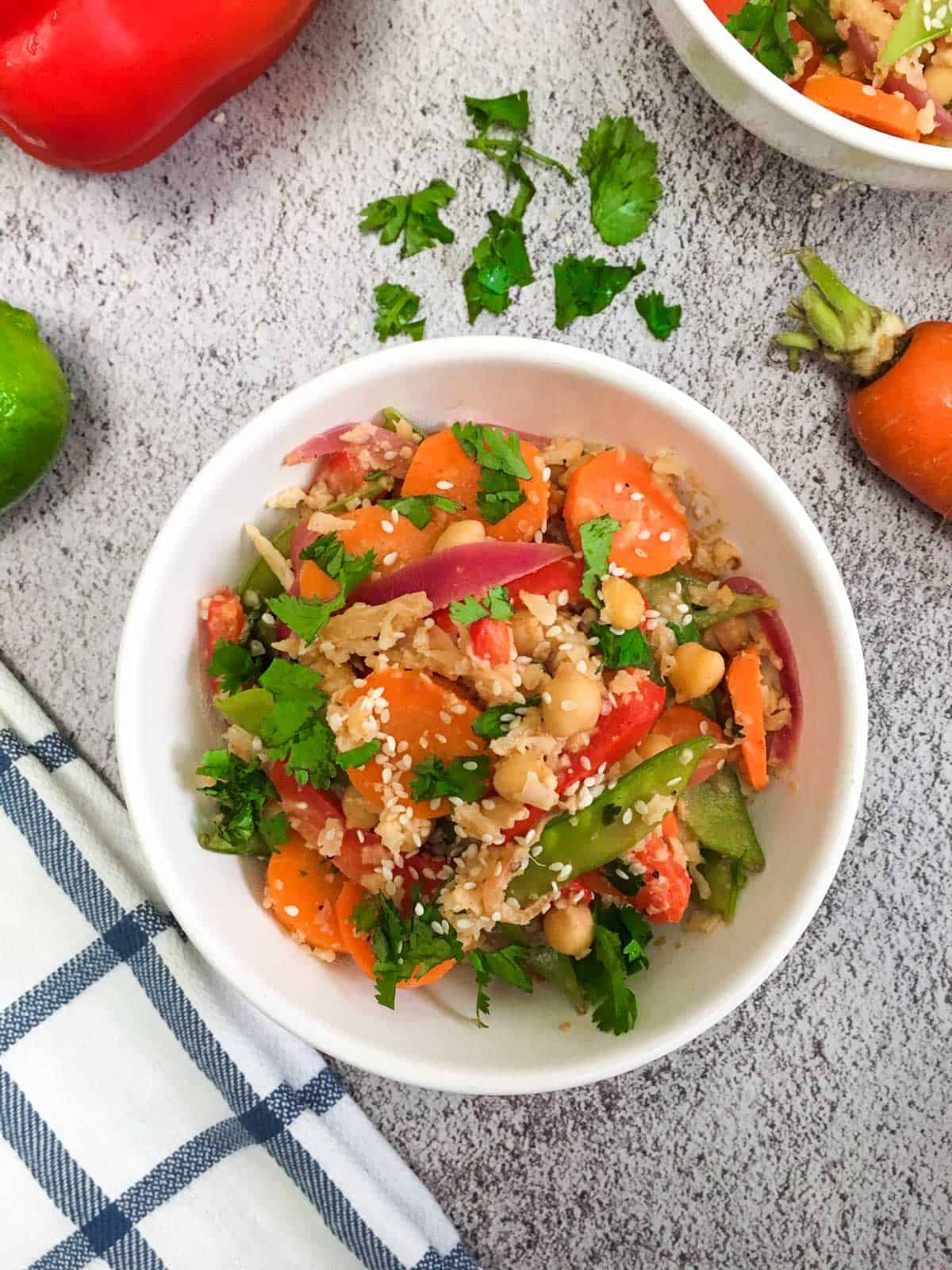 White bowl with rice, purple onion, carrots, chickpeas, and green peas with chopped green herbs.