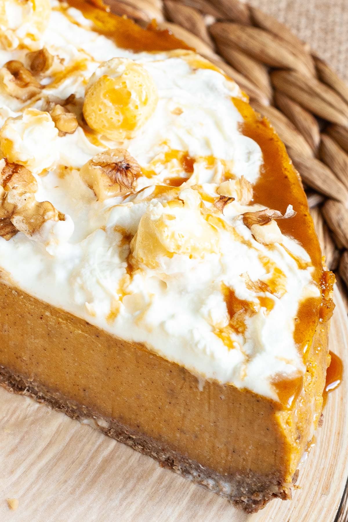 Part of an amber brown cheesecake topped with whipped cream, caramel sauce and chopped nuts.