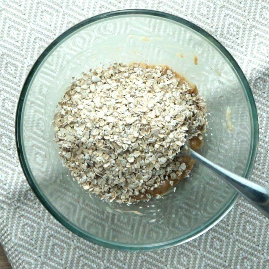 A glass bowl with mashed bananas topped with a heap of rolled oats.