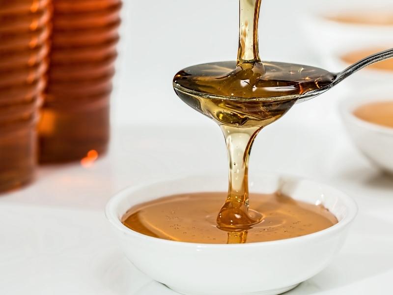 Amber brown syrup is pouring through a spoon into a small white bowl.