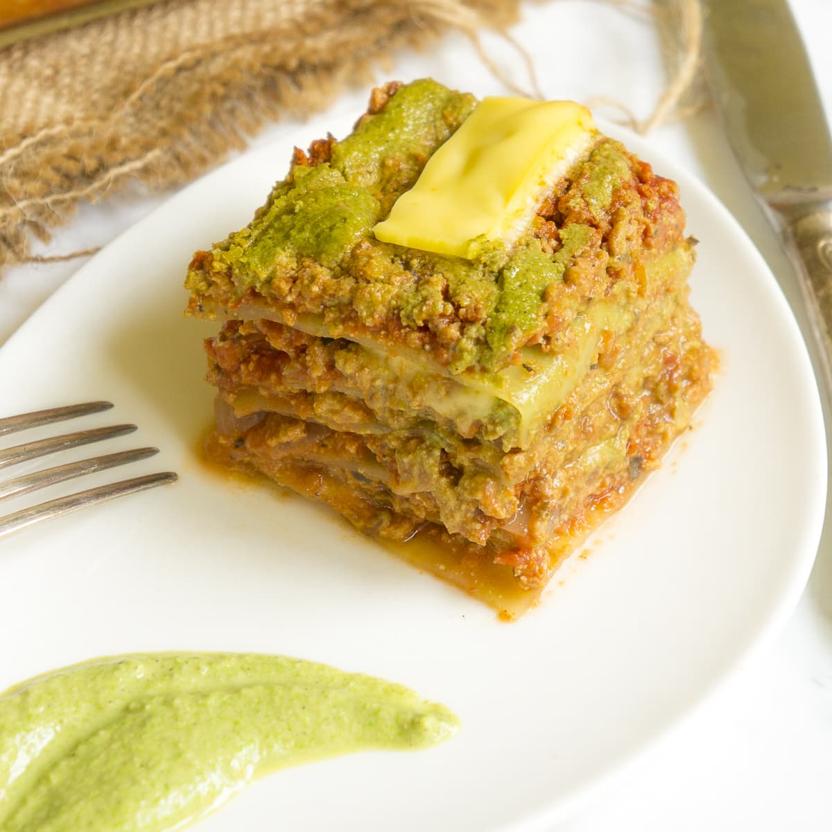 One portion of green red lasagna with cabbage leaves served on a white plate.