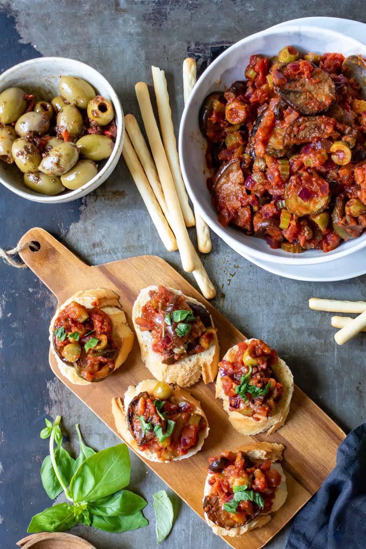 Table with a bowl of caponata, and a tray of crostini topped with caponata siciliana. 
