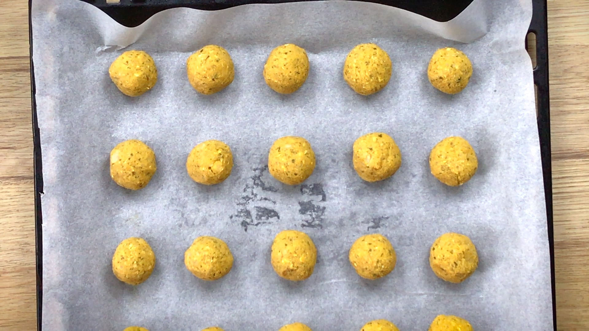 Yellow balls lined on a parchment paper in a sheet pan.
