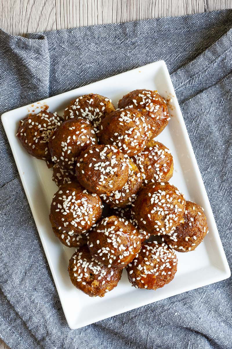 White plate with several brownish-redish balls on top of each other sprinkled with sesame seeds.