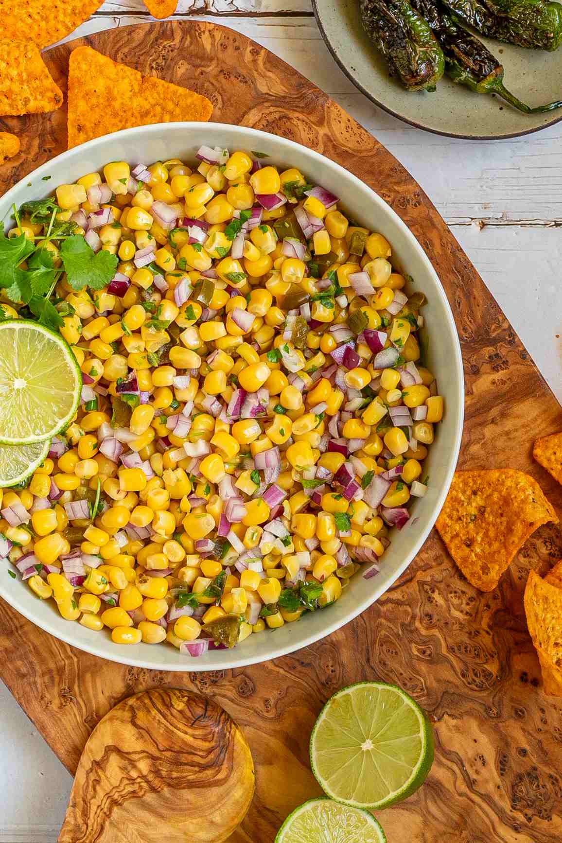 Corn salsa in a large white bowl with lime slices and nachos.