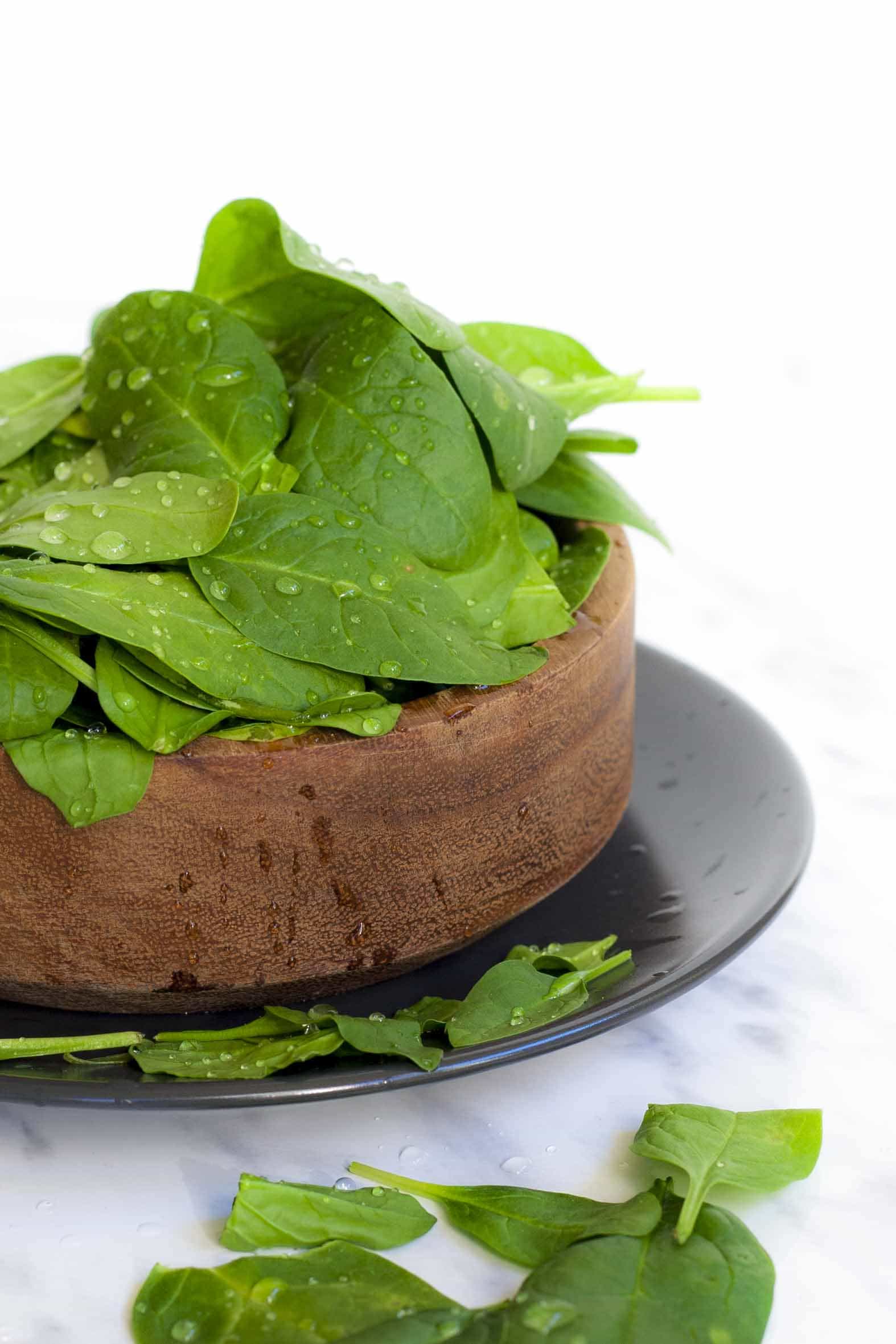 Bowl of french spinach leaves with water drops as they were freshly washed. The main ingredient of our vegan spinach soup recipe.