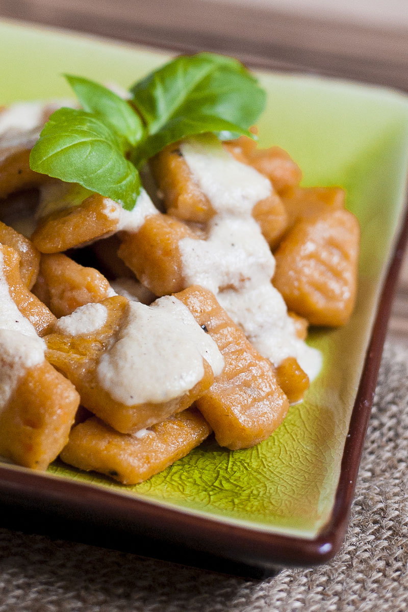 Orange rectangular-shaped pasta drizzled with white sauce on a green plate.