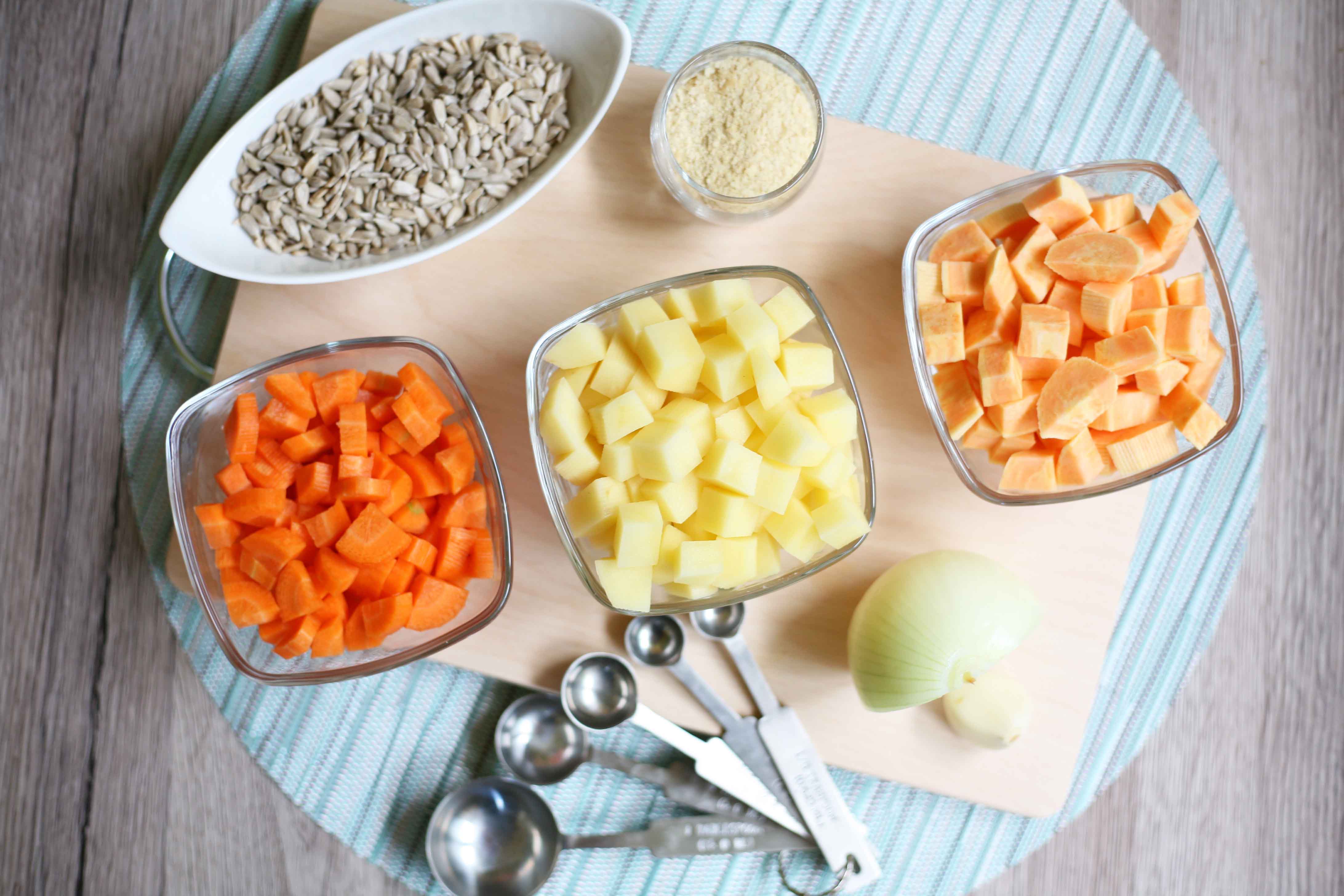 All ingredients measured in small bowls diced carrots, diced sweet potato, diced potato, sunflower seeds, half onion, clove of garlic and nutritional yeast