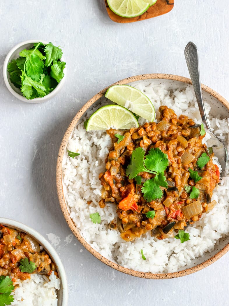 Vegan Eggplant and Lentil Curry on top of white rice with lime wedges and cilantro.
