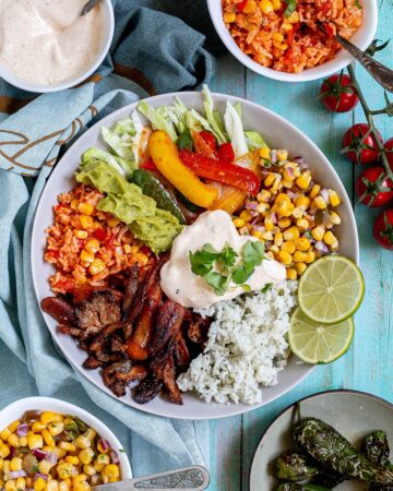White bowl with cilantro lime rice, corn salsa, mushroom fajitas, guacamole, fajitas veggies and chipotle mayo.