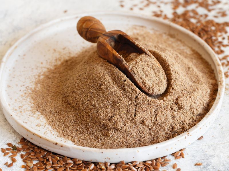 A white plate with light brown powder. Flax seeds are around it.