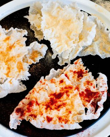 Several puffed rice paper sheets sprinkled with different spices red yellow and brownish on a black plate