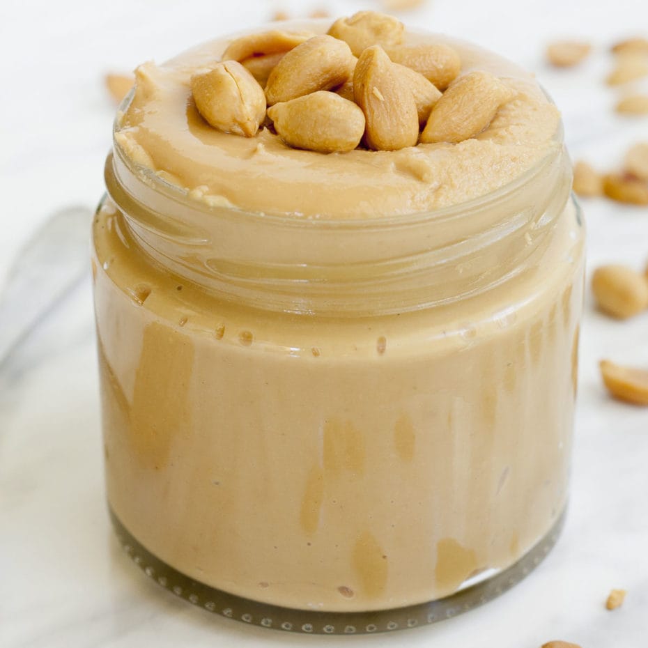A small glass jar with light brown paste topped with peanuts. 