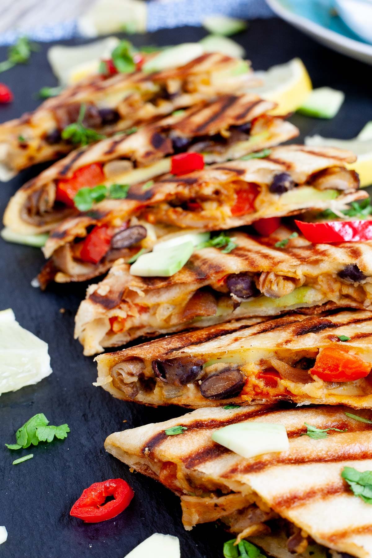 Several quesadilla triangles filled with black beans, red pepper, avocado slices sprinkled with fresh cilantro in a black board