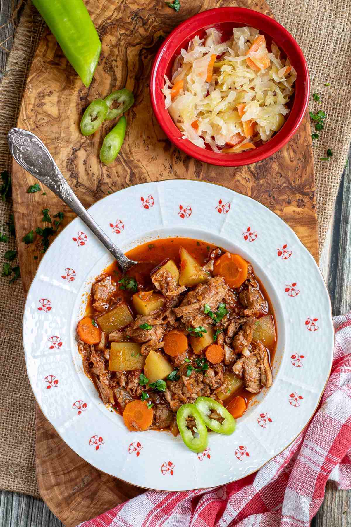 A white plate with Hungarian Goulash on a wooden table.