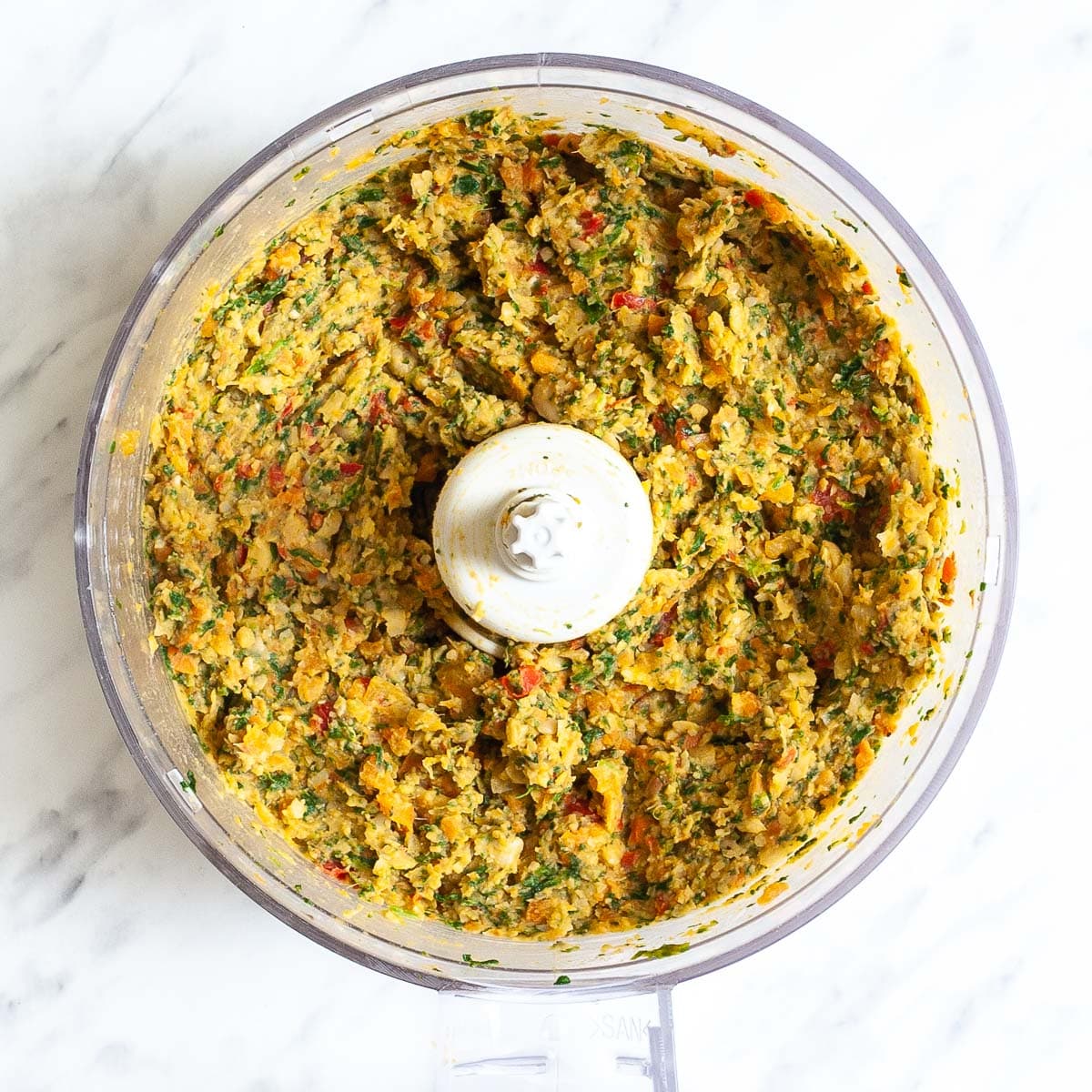 Food processor with red, yellow, and green crumbly puree. 