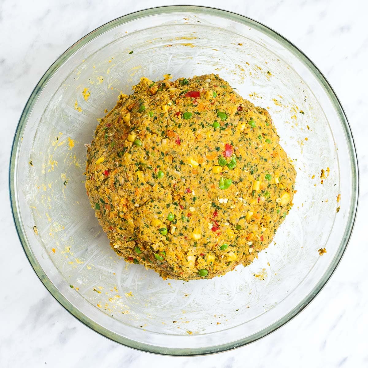 A glass bowl with red, yellow, green veggie ball dough forming a large ball. 