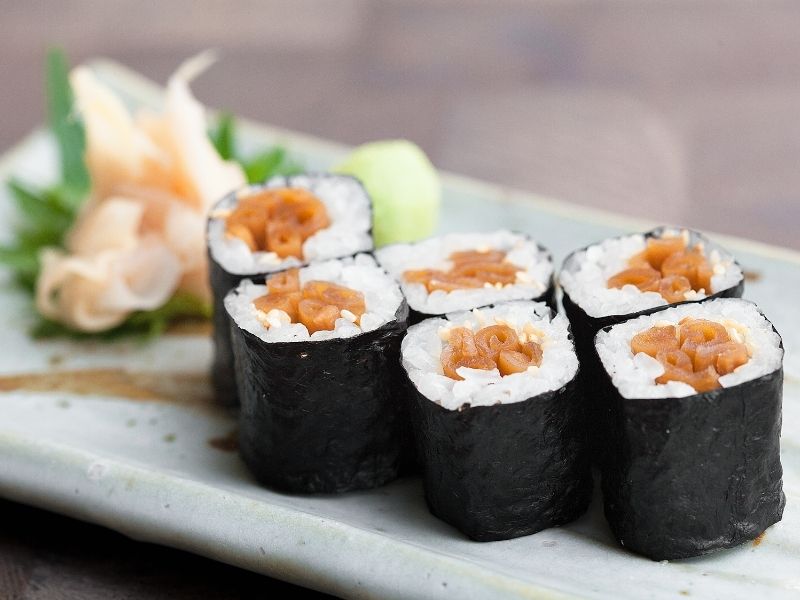 6 sushi rolls on a plate with brown filling and rice wrapped in seaweed sheets 