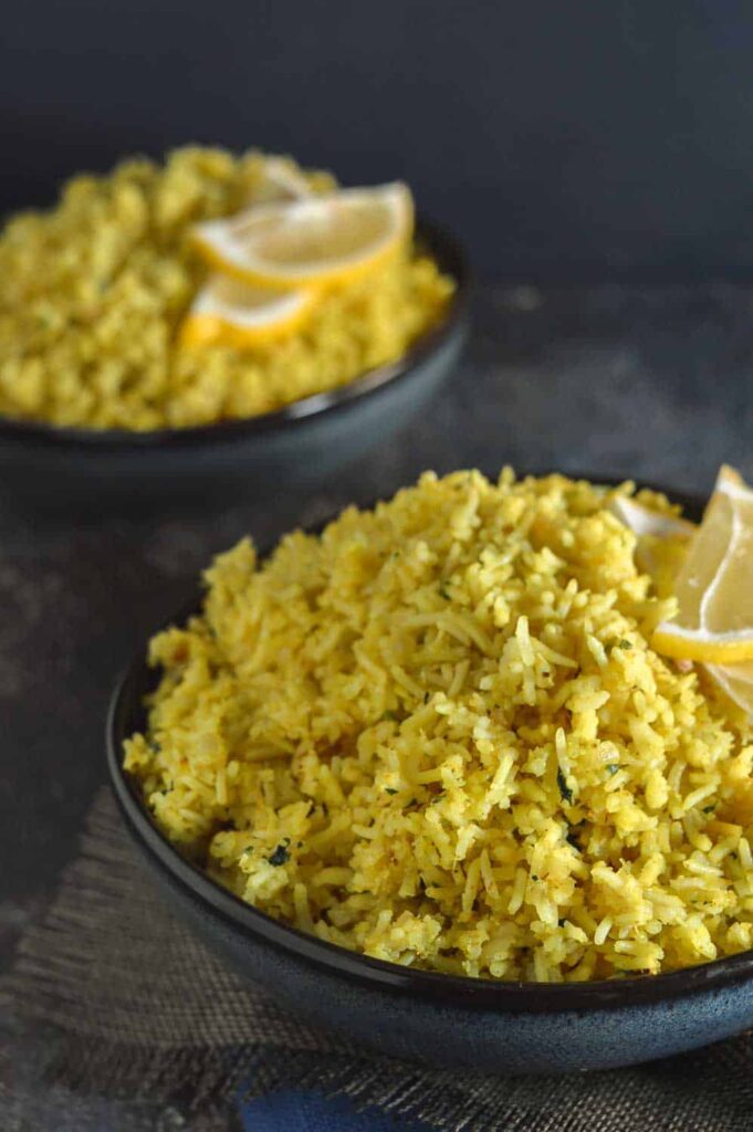 Two navy bowls of yellow rice with lemon slices on top.