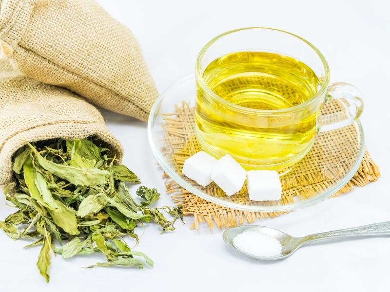 Light yellow in a glass cup and a bag of green stevia leaves
