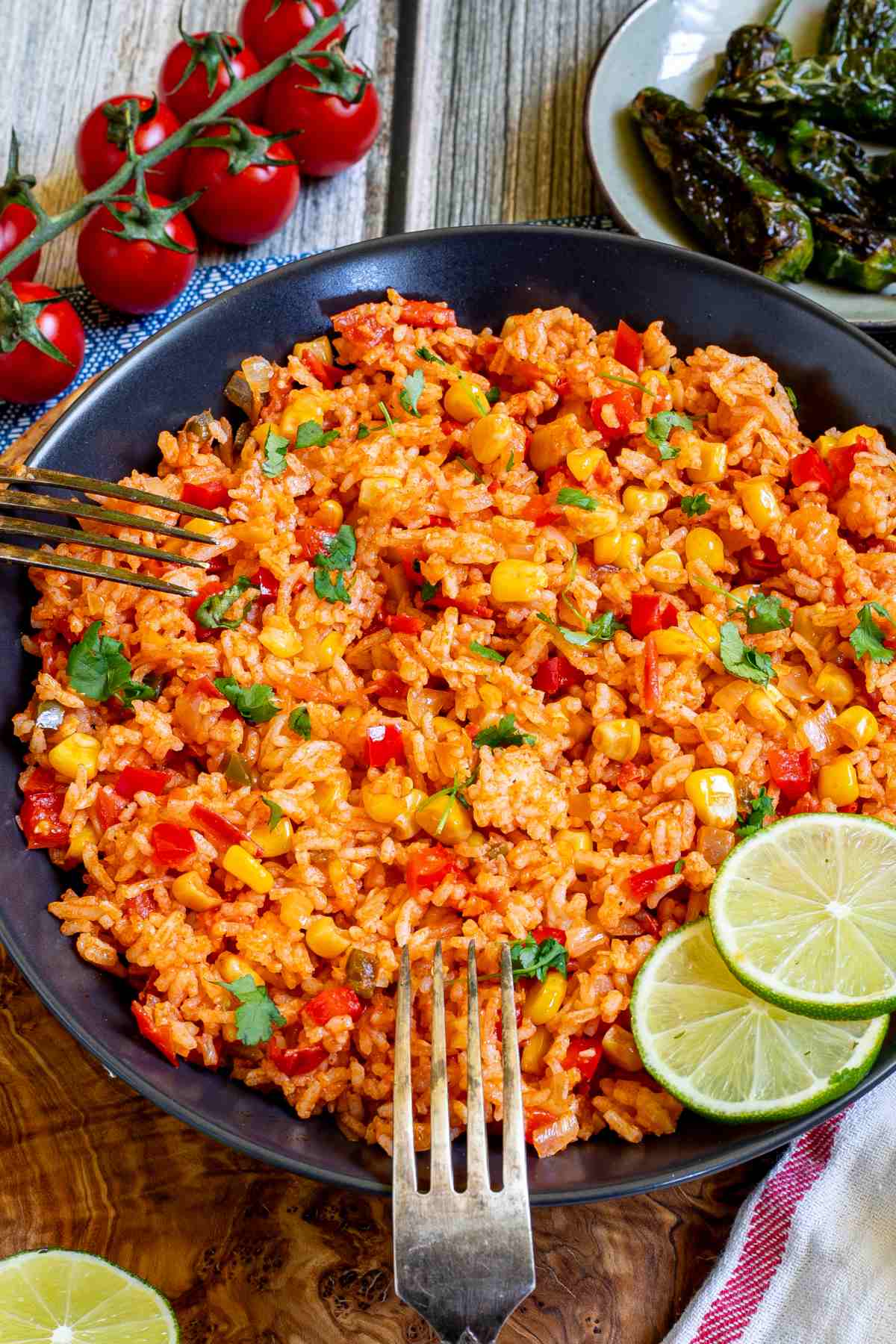 Orange rice with corn, tomato, and parsley in a black bowl. Two forks are placed on the edge of the bowl