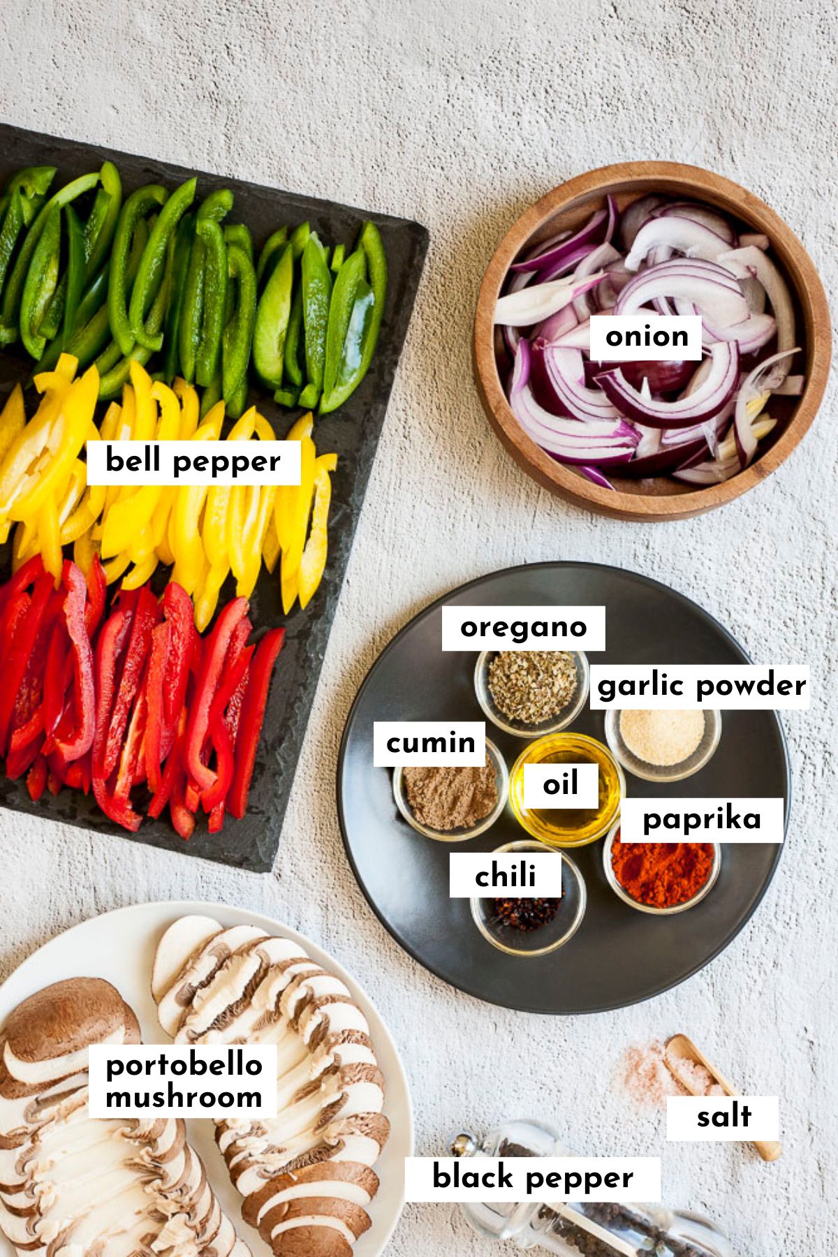 The ingredients of fajita veggies in different plates. The spices in small glass bowls, the colorful bell peppers slices on a black board. Purple onion slices in a wooden bowl. And mushroom slices one white plate