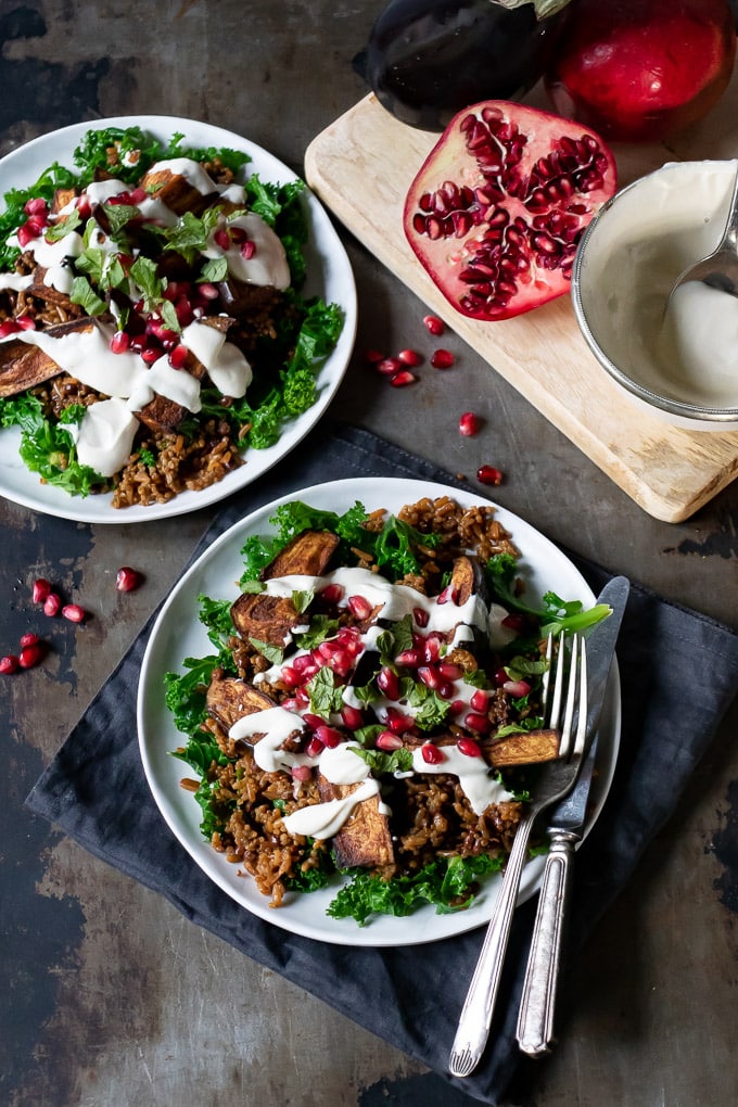 Two plates of Persian salad topped with roasted aubergines.

