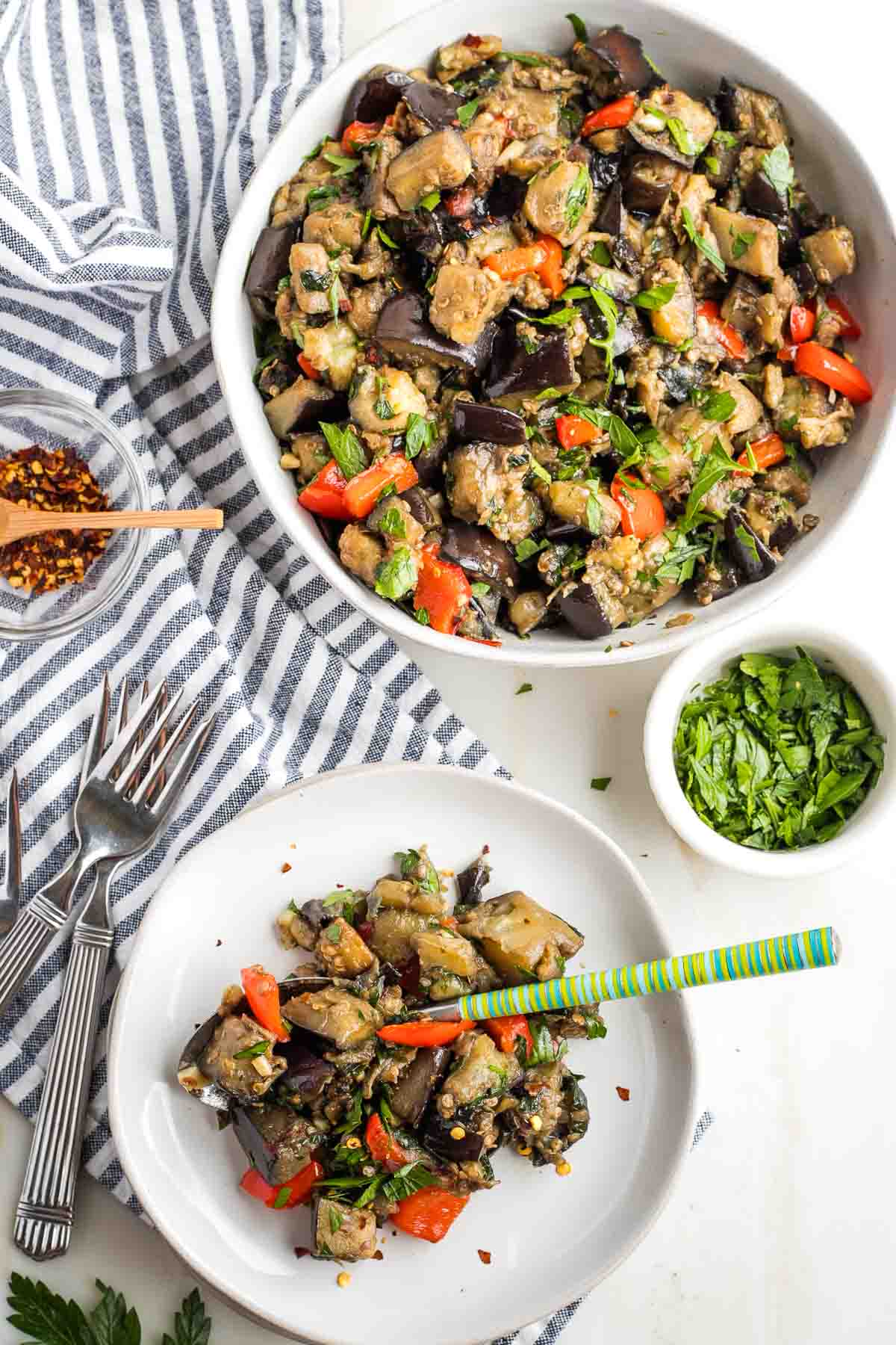 Big bowl of eggplant salad with colorful red peppers and fresh parsley and a small plate of same. 
