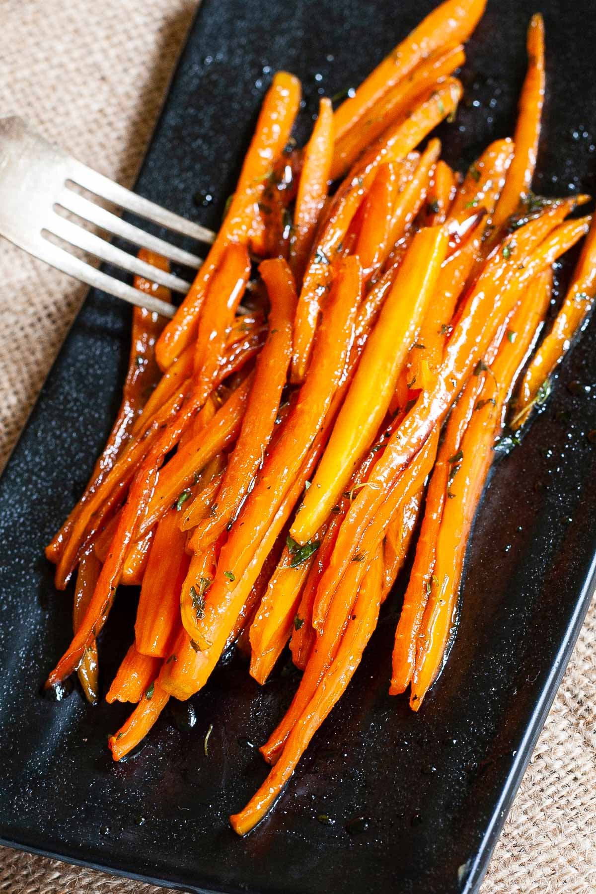 Black rectangular plate with matchstick carrots in glaze. A hand is holding a fork and taking some from the top.