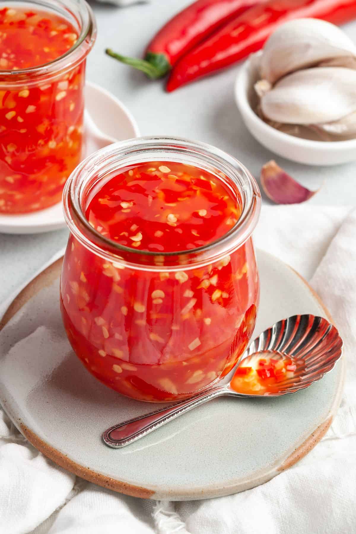 Up close shot of small pot of sauce, sitting on a saucer with a spoon on the side, and another pot of sauce behind it. 
