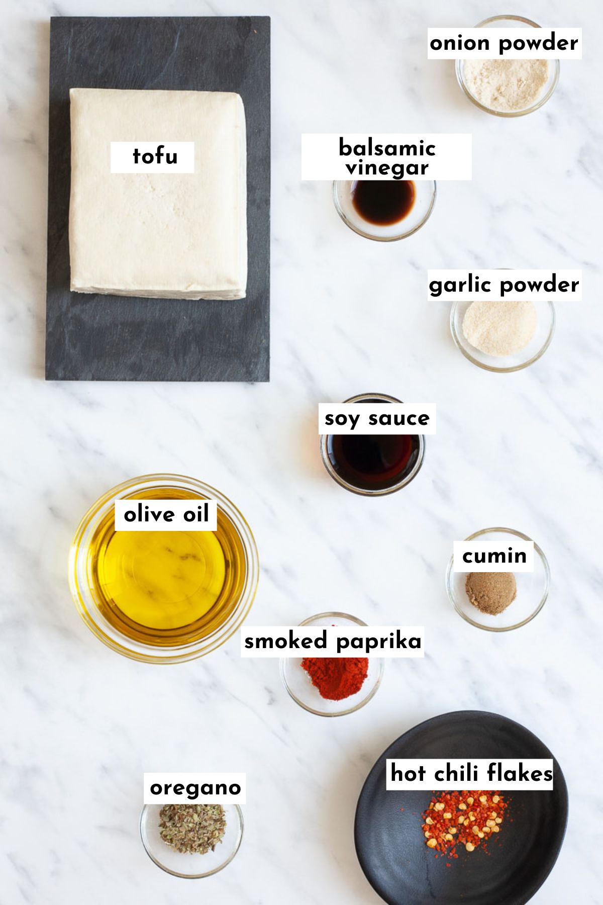 All ingredients for a tofu steak are separated into lots of glass bowls: 2 bowls with dark black sauce, one with oil, 4 with light yellow-white powder and one with a red chili flakes. And there is a block of firm tofu on a black plate