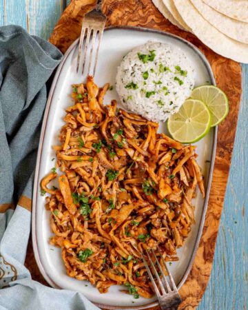 Thin juicy golden brown oyster mushrooms shred sprinkled with chopped green herbs on a light blue tray served with a scoop of rice.