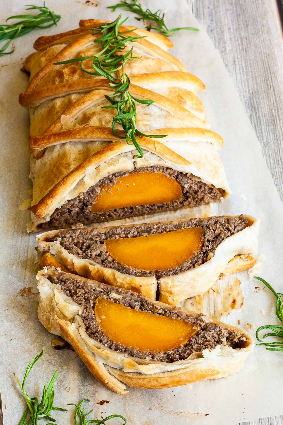 2 slices of vegan wellington on the side. Yellow squash with brown puree around wrapped in a pastry shell. Green herbs are around.