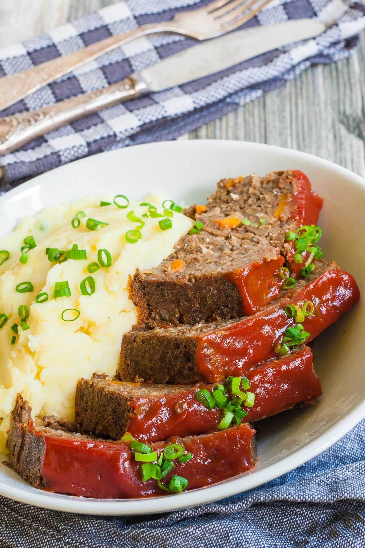 4 slices of lentil loaf glazed with a red sauce served in a large bowl with mashed potatoes and chopped scallions.