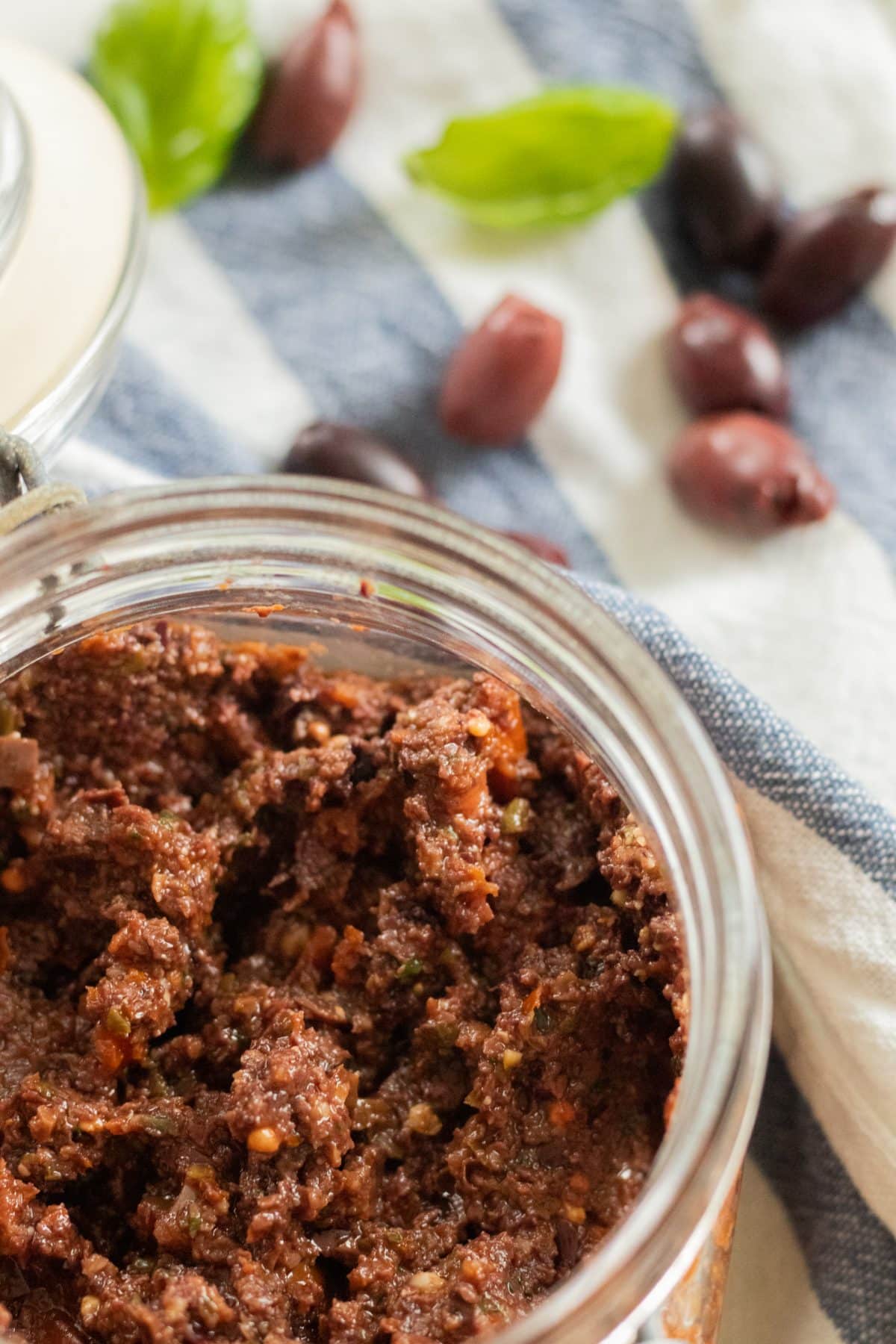 top view of a jar with olive tapenade and olives and basil in the background.