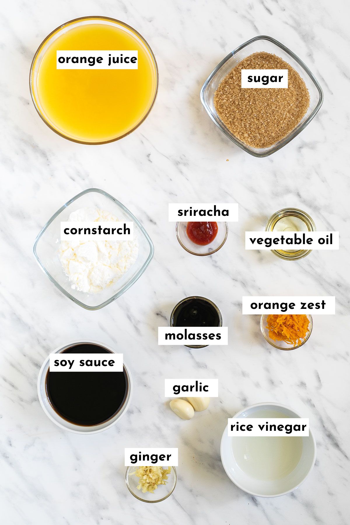 Ingredients of vegan orange chicken are in small glass bowls like orange juice, sugar, corn starch, molasses, soy sauce, orange zest, oil, vinegar and garlic, ginger.