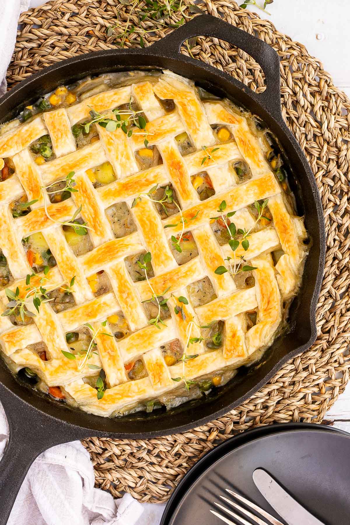 Cast iron skillet with veggie stew topped with puff pastry in a lattice pattern.