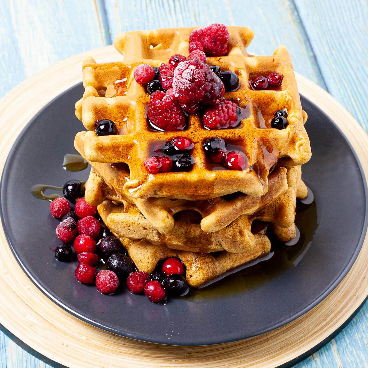 Black plate with a stack of waffles topped with mixed berries and maple syrup