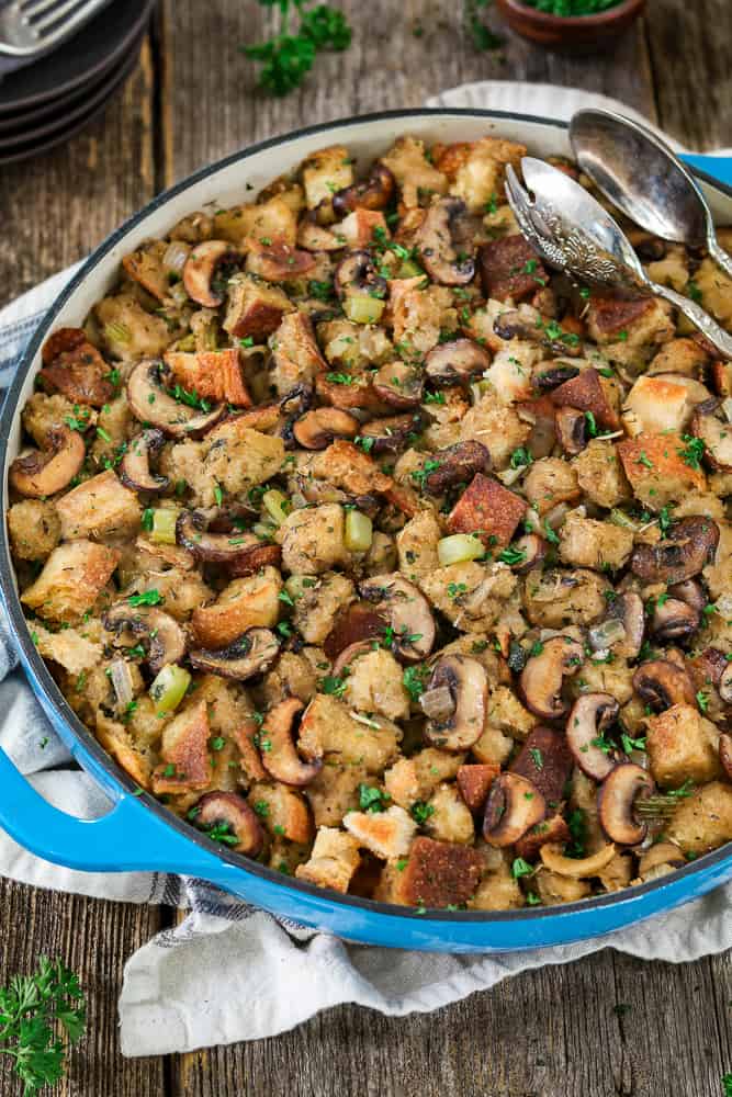 closeup photo of fully baked Vegan Sourdough Bread Stuffing in a blue casserole dish. Silver serving spoon on top. 