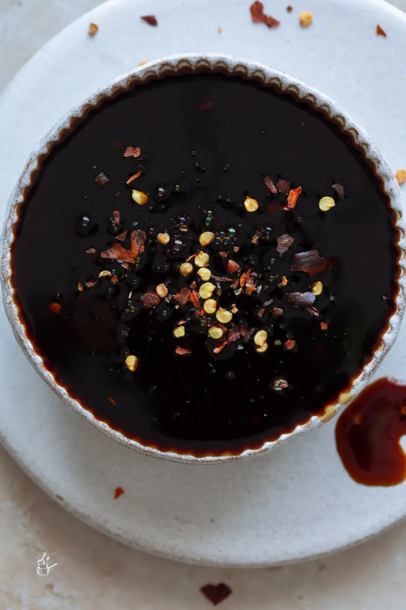 A small bowl of asian zing sauce placed on a round white tray. 
