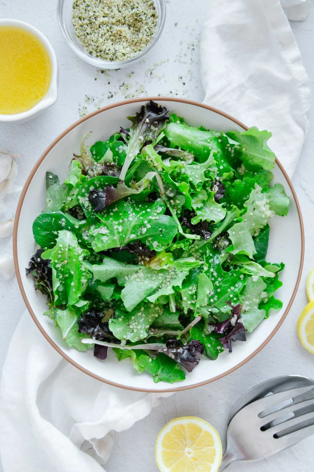 A bowl of fresh greens with homemade dressing on a white background.