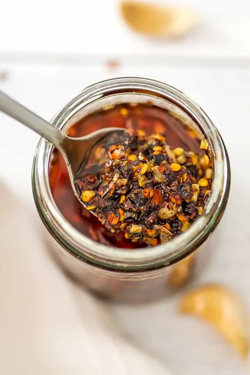 Large spoonful of chili garlic oil being spooned out of a jar. 
