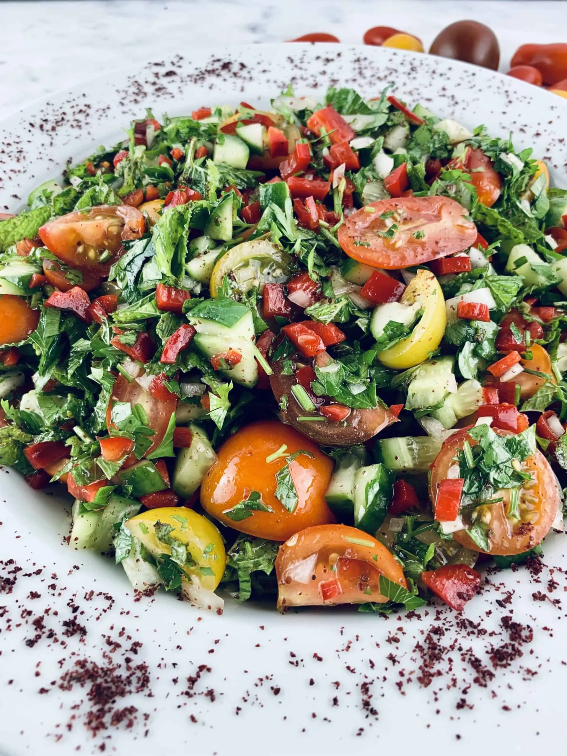 Close-up of Sumac Salad in a white salad platter, with sumac powder around the edges with coloured cherry tomatoes on the side.